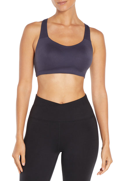 A woman modeling a dark gray scoop-neck sports bra and black high-waisted leggings against a plain white background. 