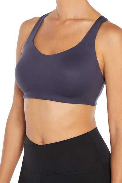 A close-up of a woman wearing a dark slate purple sports bra and black high-waisted leggings against a plain white background.  