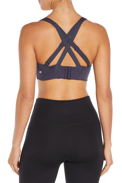 Rear view of a woman wearing a dark gray sports bra with crisscross back straps and black high-waisted leggings against a white background.  