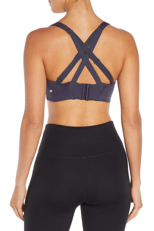 Rear view of a woman wearing a dark gray sports bra with crisscross back straps and black high-waisted leggings against a white background.  #color_graphite