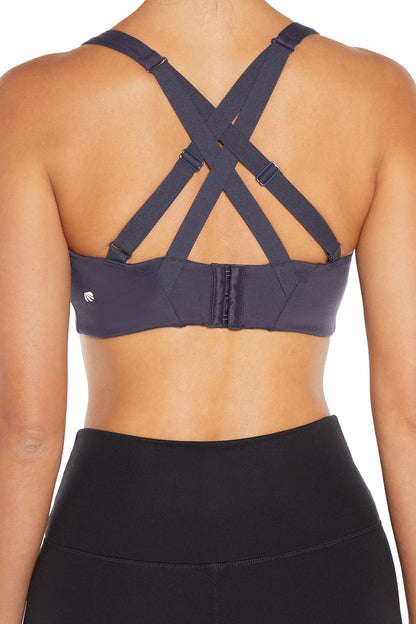Rear view of a woman wearing a dark gray sports bra with crisscross back straps and black high-waisted leggings against a white background.  