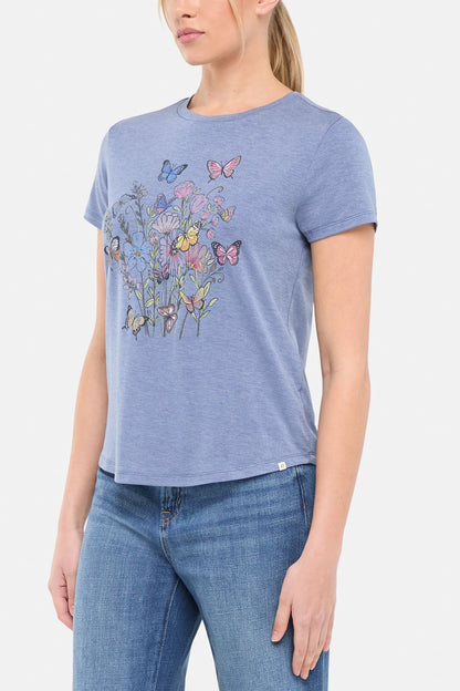 Side view of woman wearing a blue t-shirt with butterflies and floral design on a white background. 