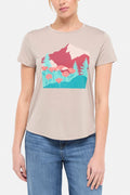 Front view of woman wearing a beige t-shirt with a graphic design of trees and poppy flowers, paired with blue jeans on white background. #color_heather-atmosphere-poppies-on-mountains