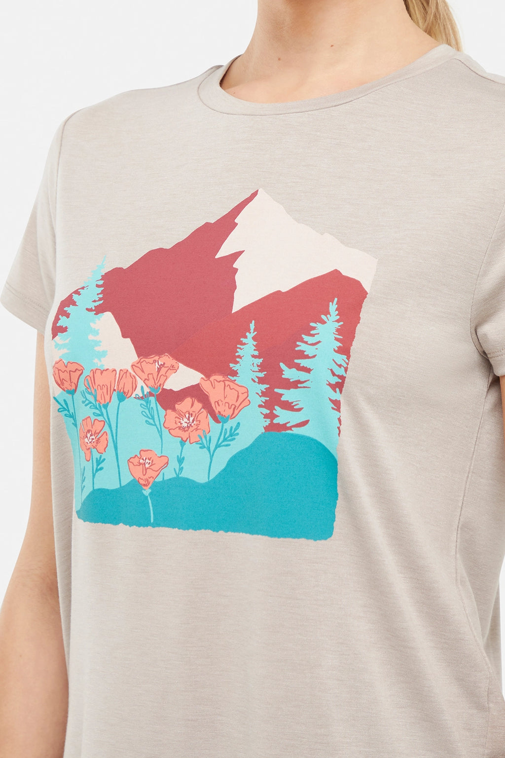 Close up view of woman wearing a beige t-shirt with a graphic design of trees mountains, and poppy flowers, paired with blue jeans on white background. #color_heather-atmosphere-poppies-on-mountains