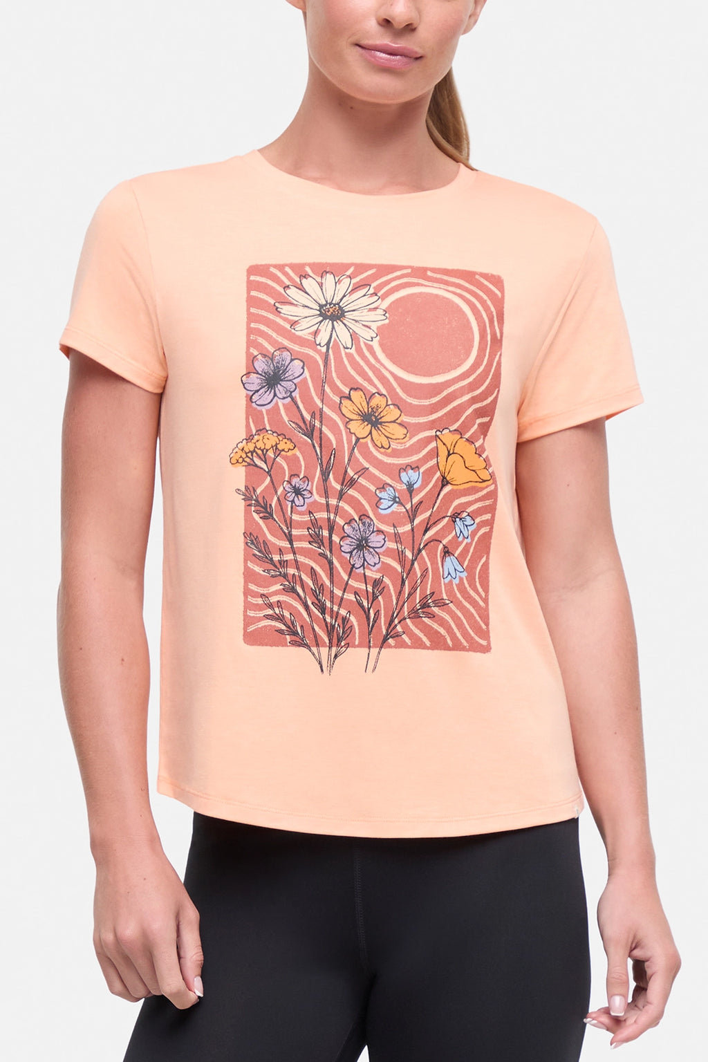 Front view of woman wearing a peach t-shirt with floral graphic on a light gray background. #color_heather-melon-ice-daisies-in-the-sun