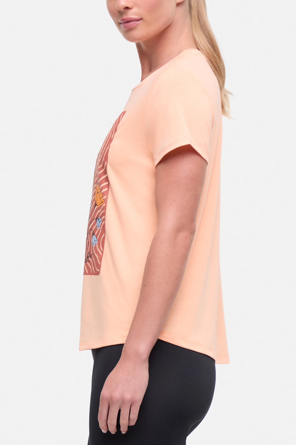 Side view of woman wearing a peach t-shirt with floral graphic on a light gray background. #color_heather-melon-ice-daisies-in-the-sun