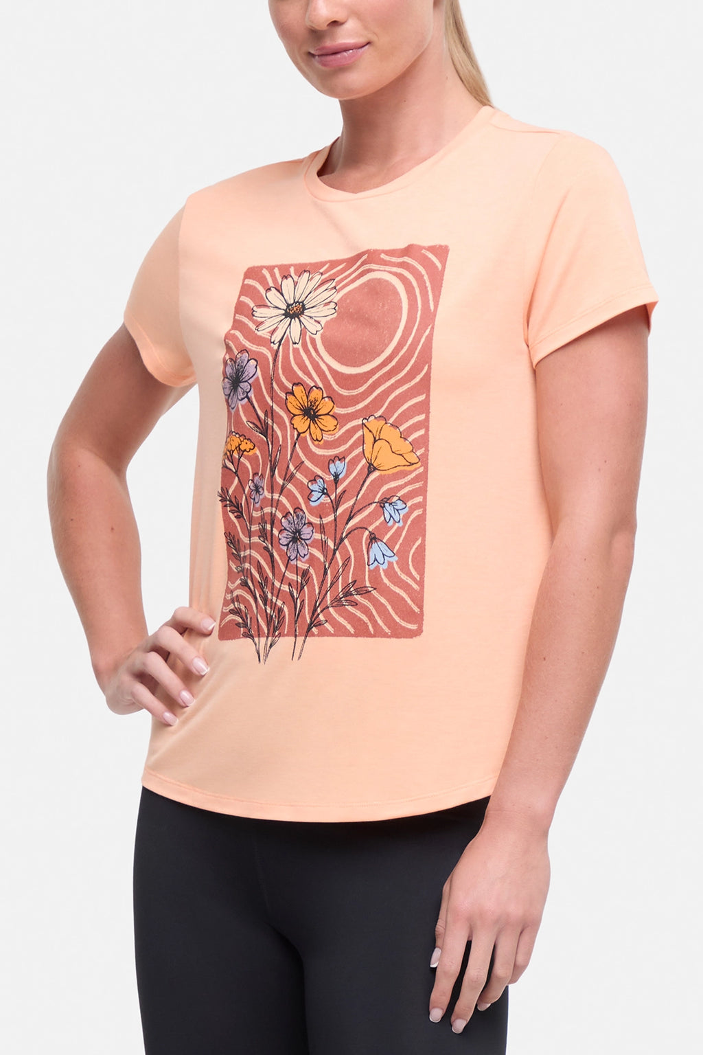 Front view of woman wearing a peach t-shirt with floral graphic on a light gray background. #color_heather-melon-ice-daisies-in-the-sun