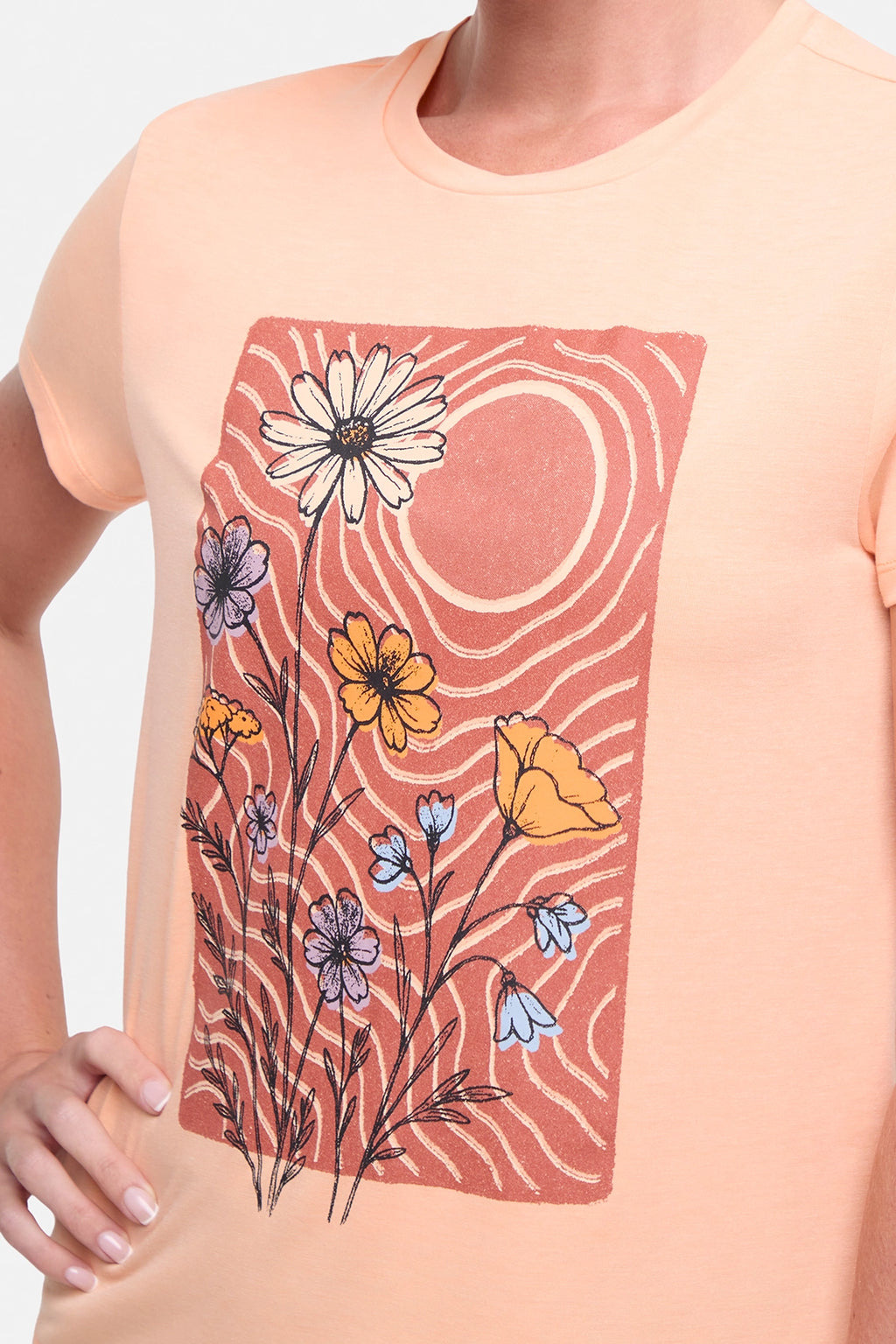 Close up front view of woman wearing a peach t-shirt with floral graphic on a light gray background. #color_heather-melon-ice-daisies-in-the-sun