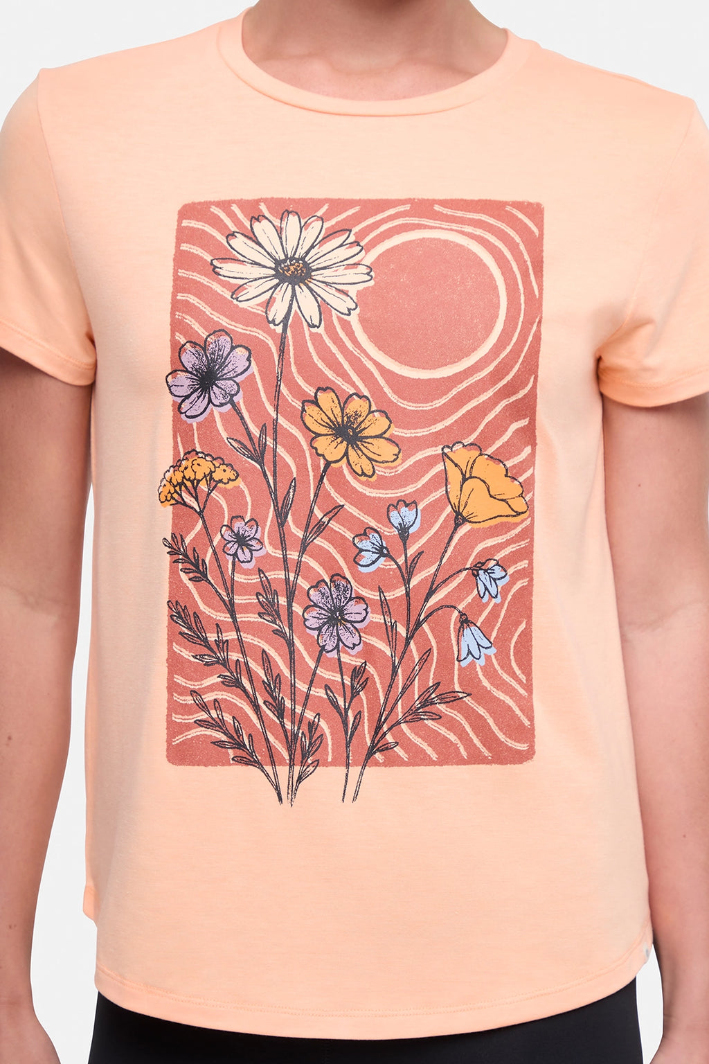 Close up front view of woman wearing a peach t-shirt with floral graphic on a light gray background. #color_heather-melon-ice-daisies-in-the-sun