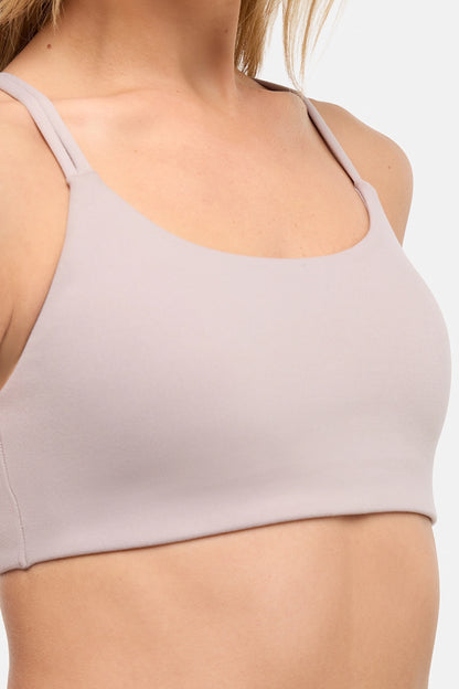 Close up front view of woman wearing a light grey-beige sports bra and white skort on a white background. 