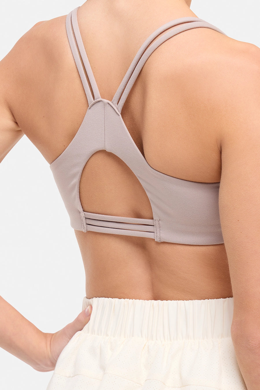 Back view of woman wearing a light grey-beige sports bra and white skort on a white background. #color_atmosphere