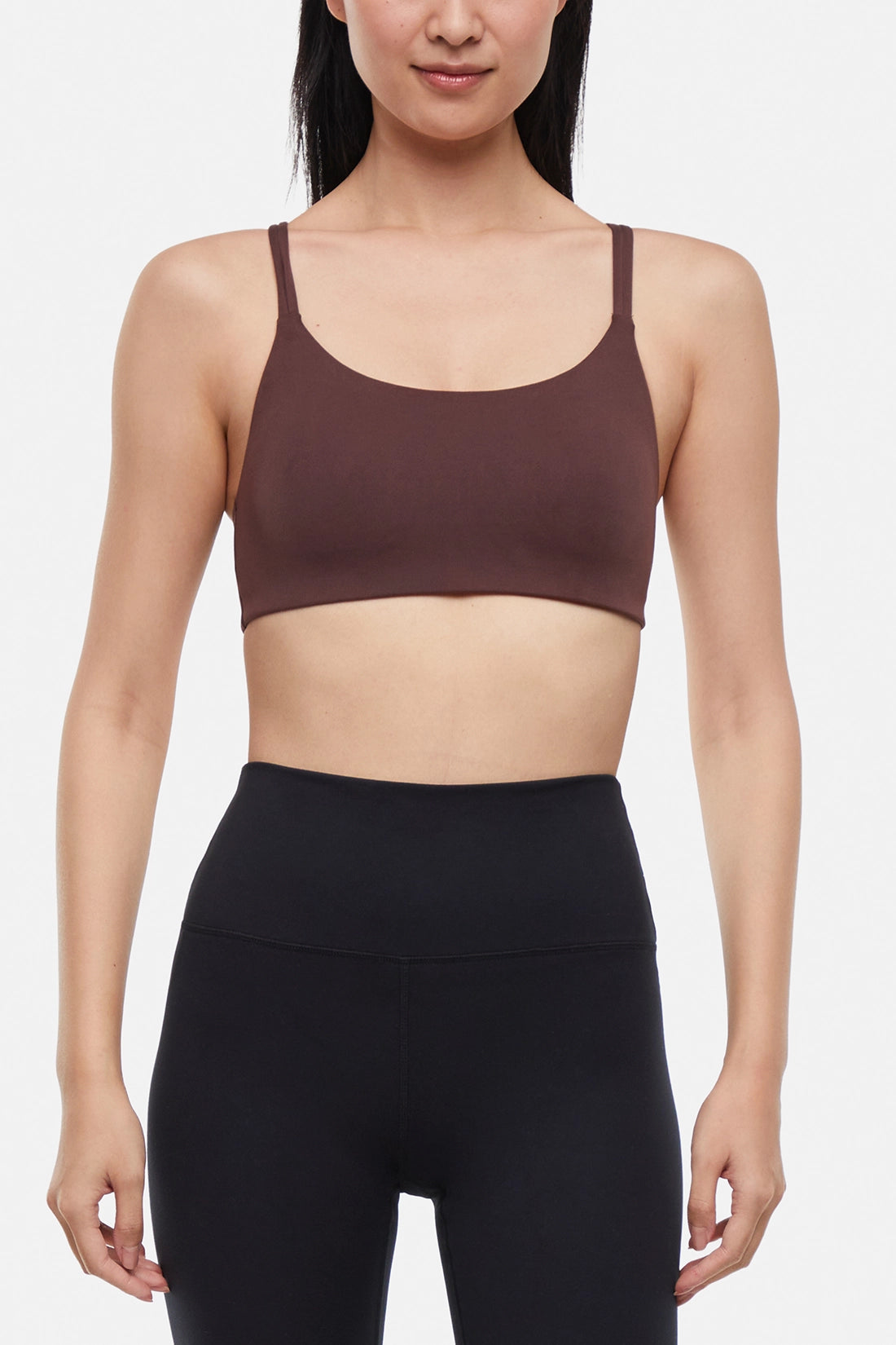 Front view of woman wearing a brown sports bra and black leggings on a white background. 