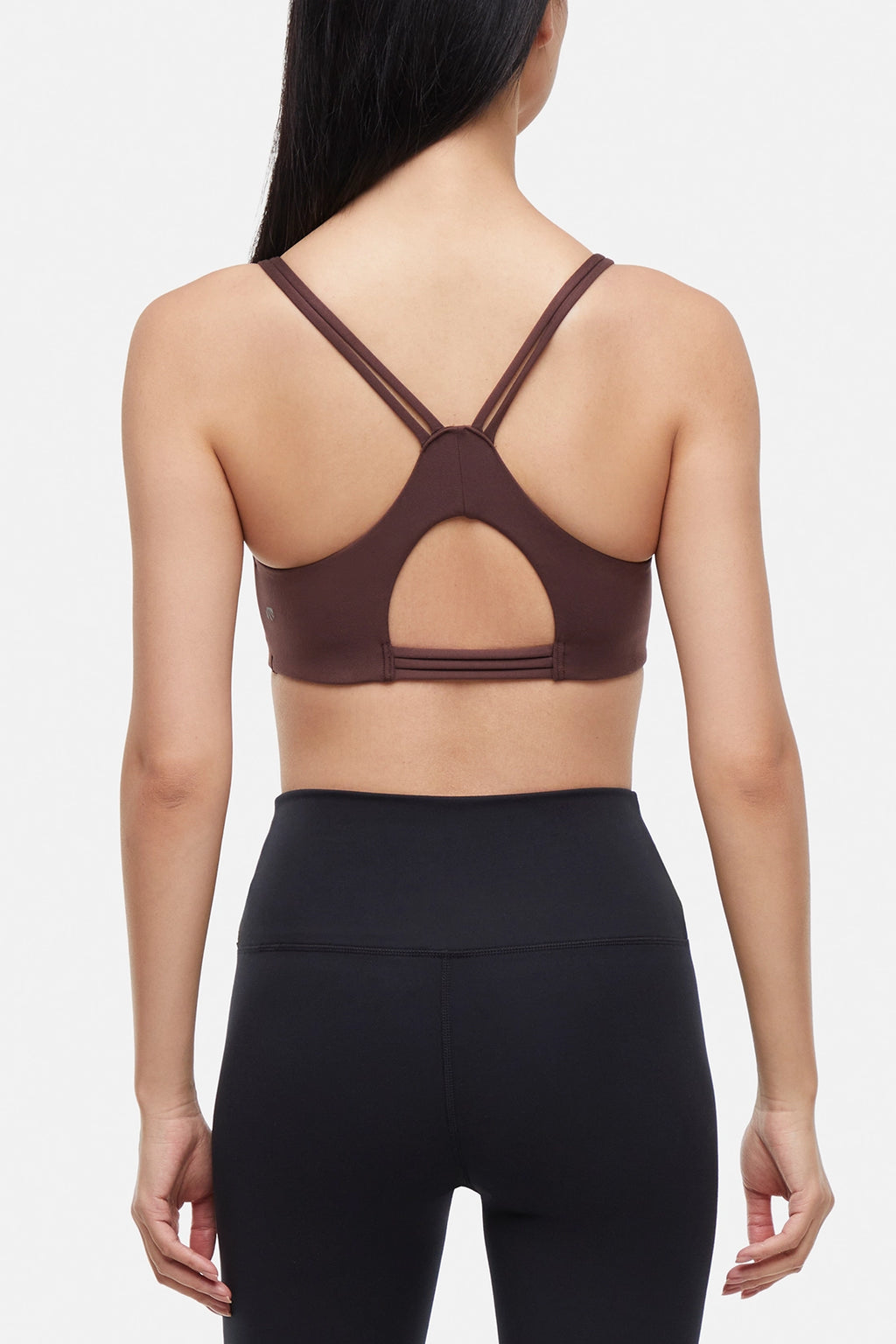 Back view of brown sports bra with crisscross straps and keyhole cutout detail on a plain background. #color_french-roast