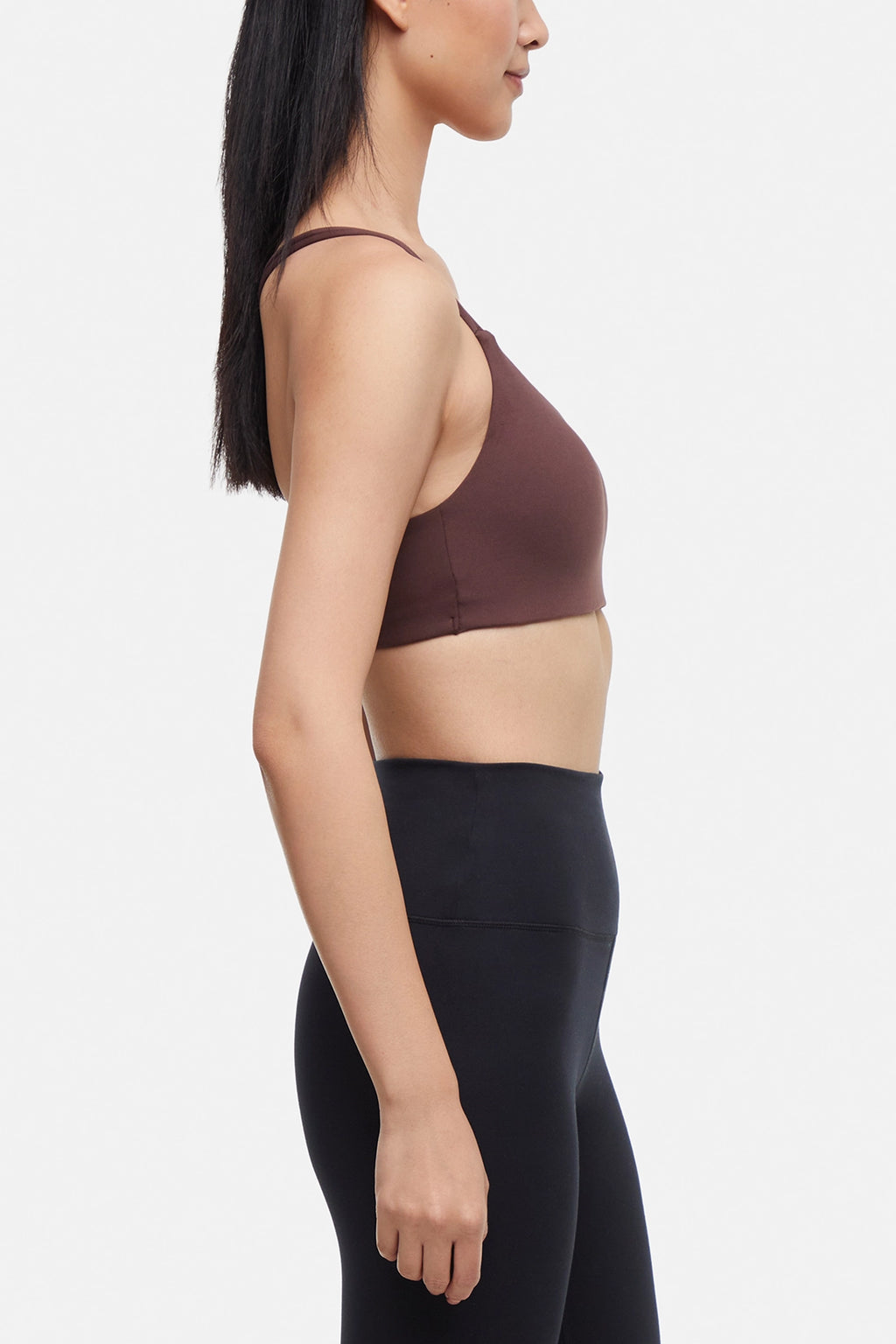 Side view of woman wearing a brown sports bra and black leggings on a white background. #color_french-roast