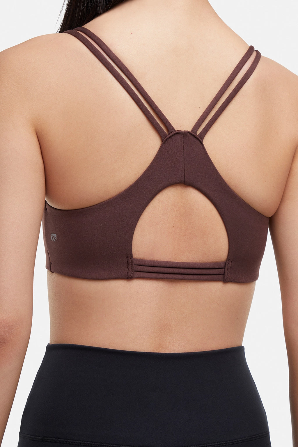 Close up back view of brown sports bra with crisscross straps and keyhole cutout detail on a plain background. #color_french-roast