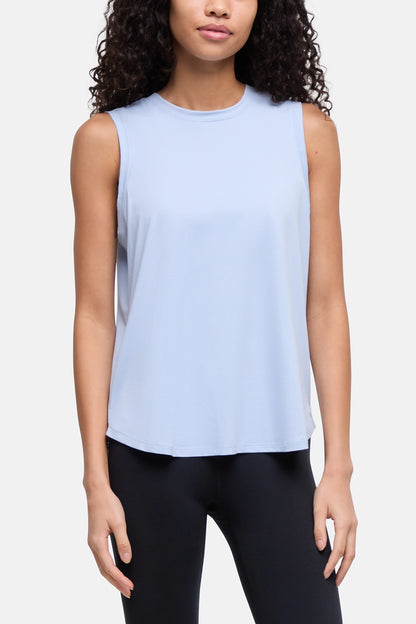 A woman wearing a light blue sleeveless crewneck tank top and black leggings, shown from the waist up against a plain light gray studio background. 