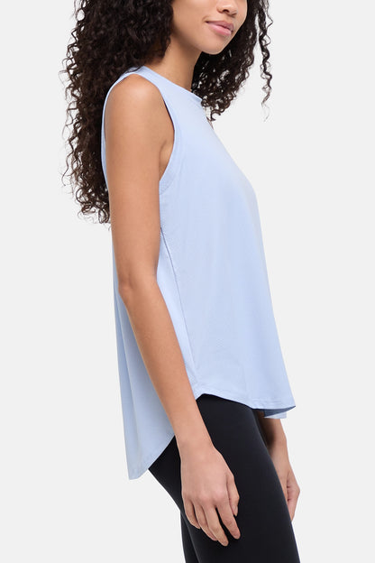 A woman wearing a light blue sleeveless high-low top and black leggings, shown in a side profile against a plain light gray studio background. 