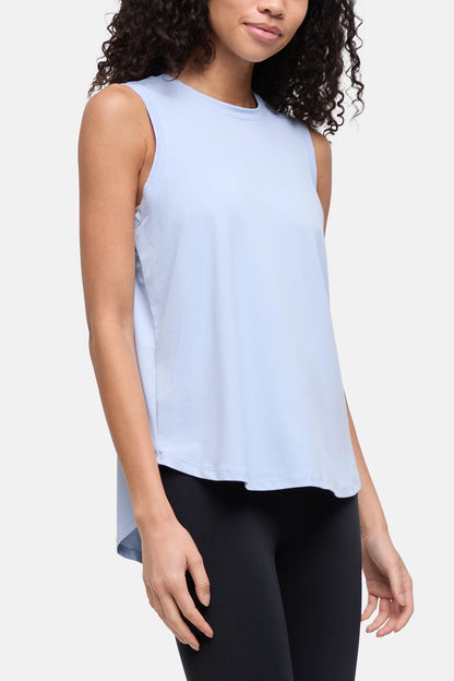 A woman wearing a light blue sleeveless high-low tank top and black leggings, shown from the waist up against a plain light gray studio background. 