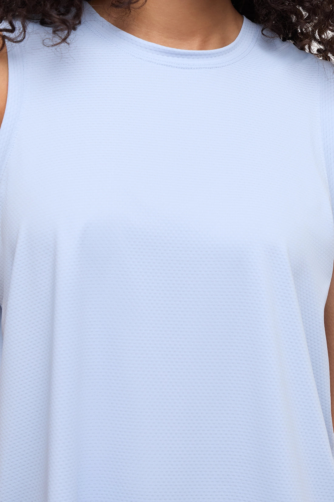 Close-up of a sleeveless athletic top in a very light icy blue color, showing the textured fabric and crew neckline on a model. 