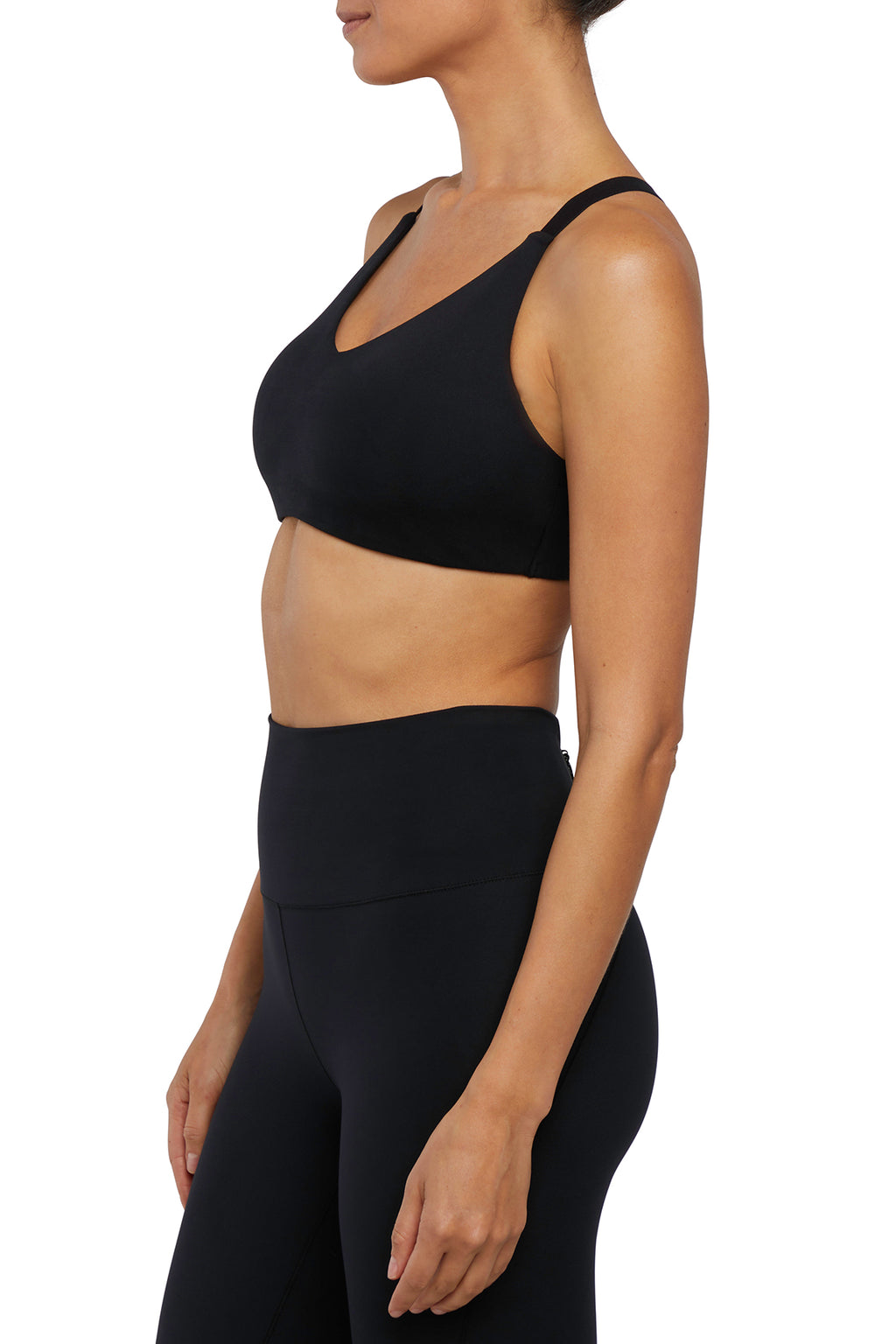 Side view of woman wearing a black sports bra and leggings on a white background. #color_black