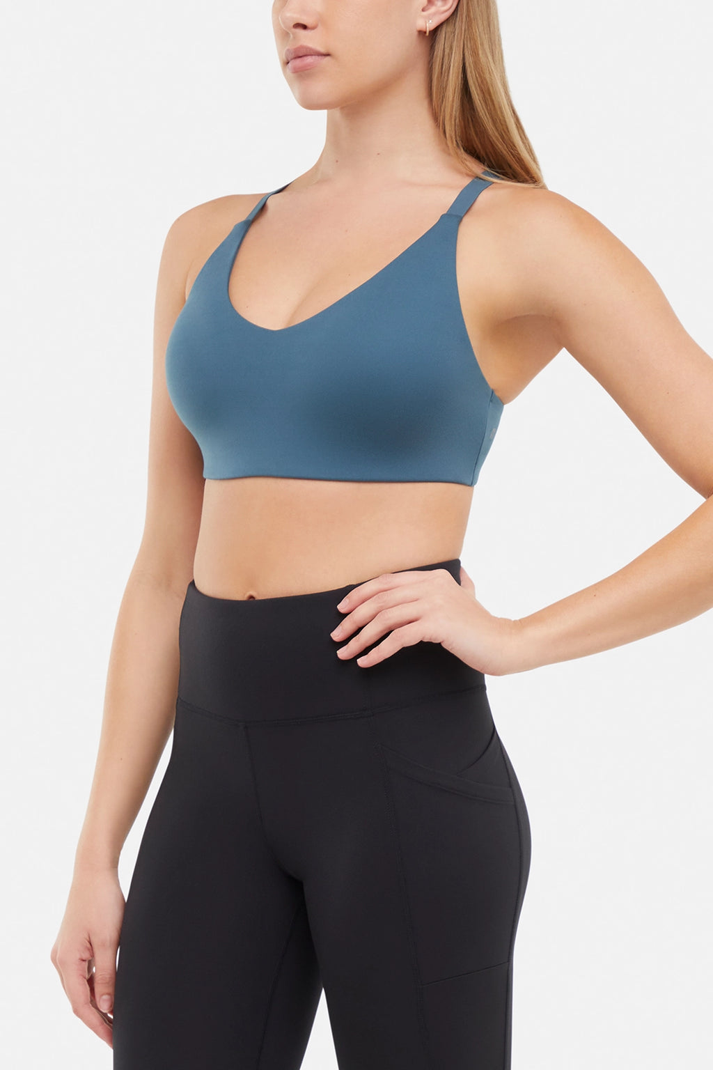 Front view of woman wearing a blue sports bra and black leggings on a white background. #color_tidal