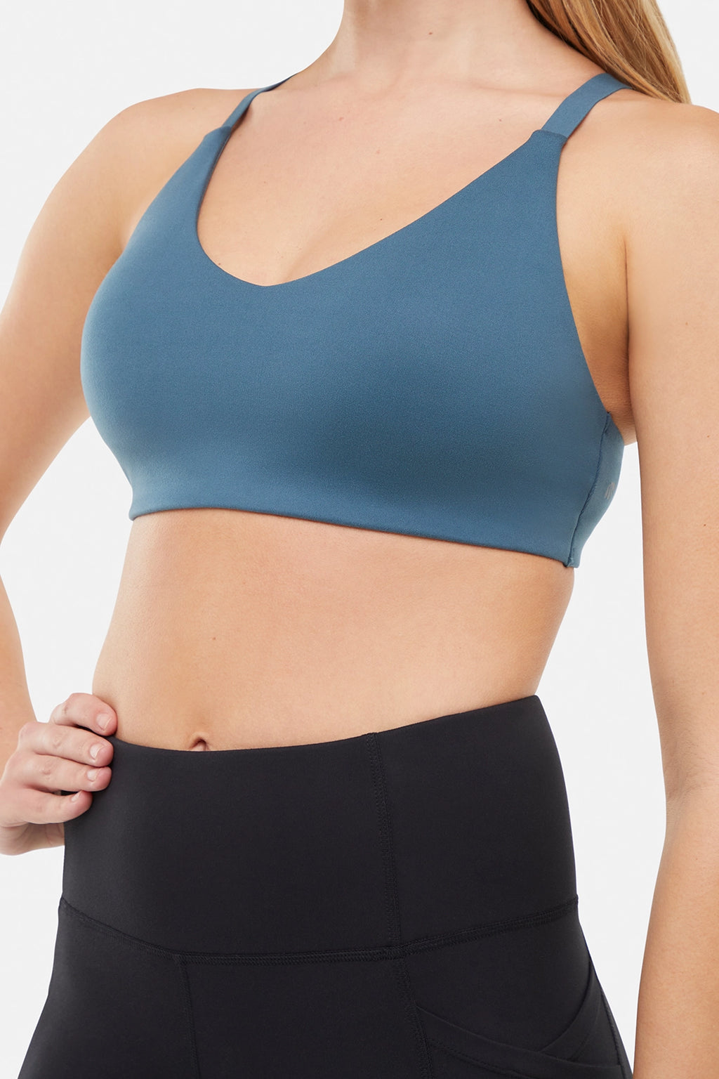Close up front view of woman wearing a blue sports bra and leggings on a white background. #color_tidal