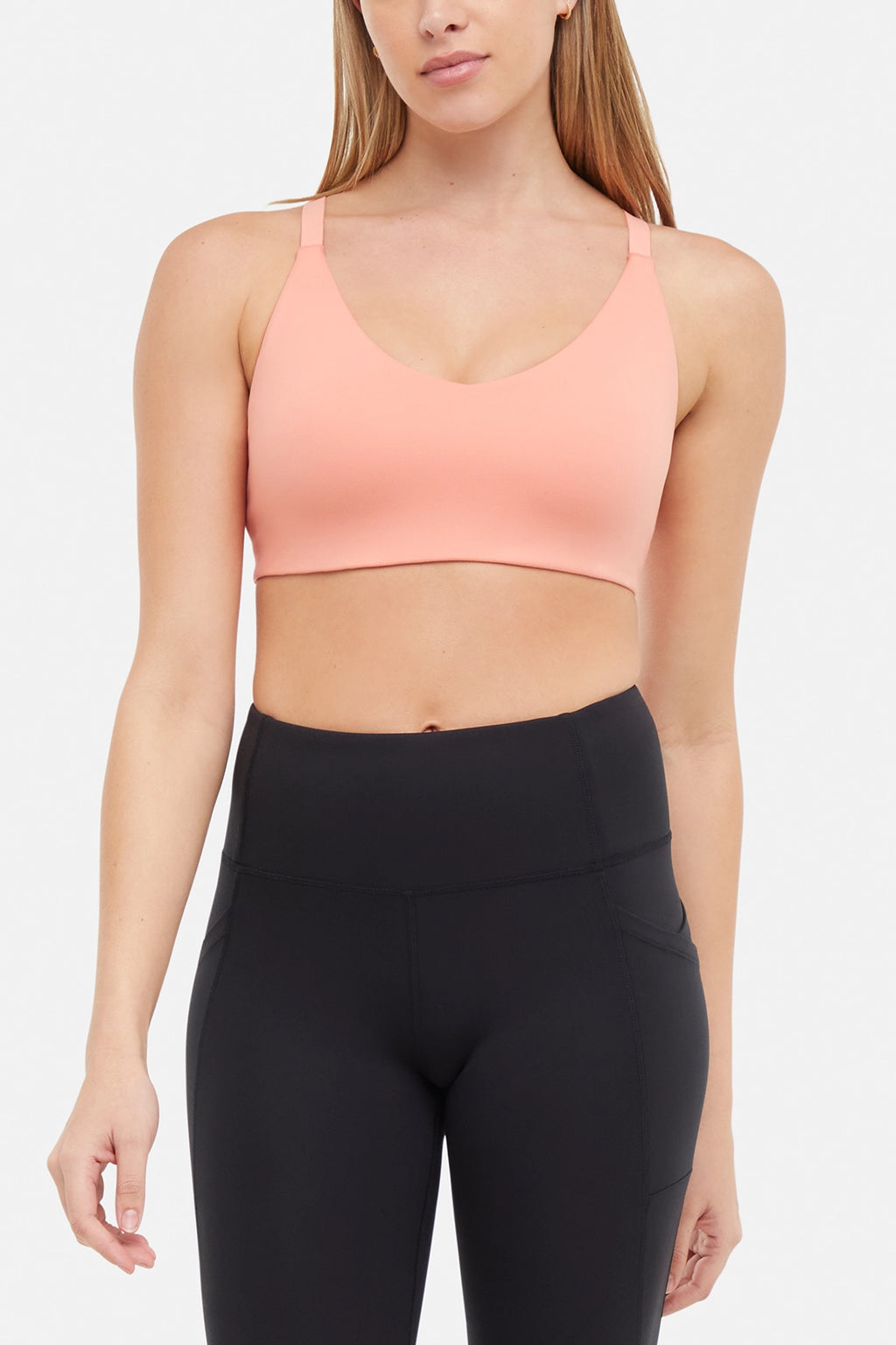 Front view of woman wearing a peach sports bra and black leggings on a white background. #color_burnt-coral