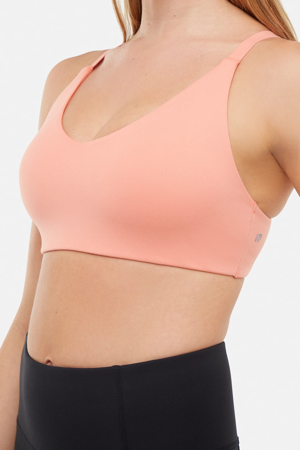 Close up front view of woman wearing a peach sports bra and black leggings on a white background. #color_burnt-coral
