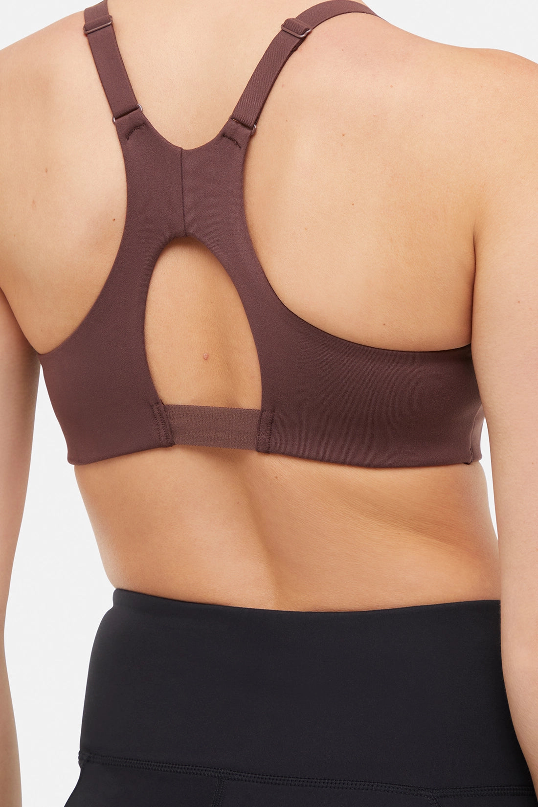 Close up back view of woman wearing a brown sports bra and black leggings on a white background. 
