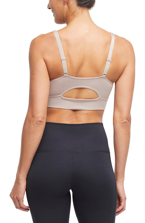 Back view of woman wearing a beige sports bra and black leggings on a white background. #color_atmosphere