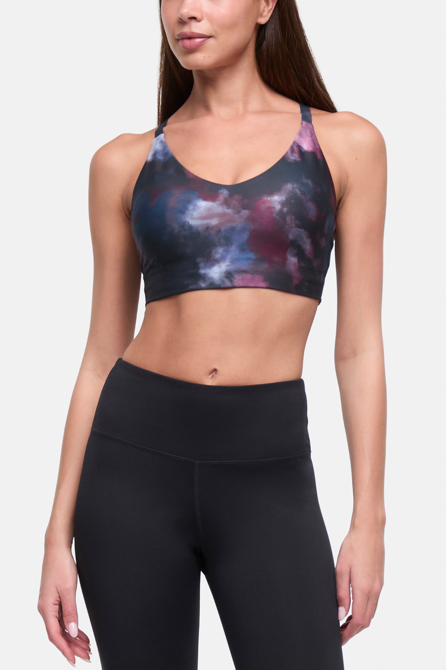 A woman wearing a sports bra with a dark galaxy print in navy, purple, and pink, paired with black high-waisted leggings, shown against a light gray studio background. #color_winetasting-clouded-cause