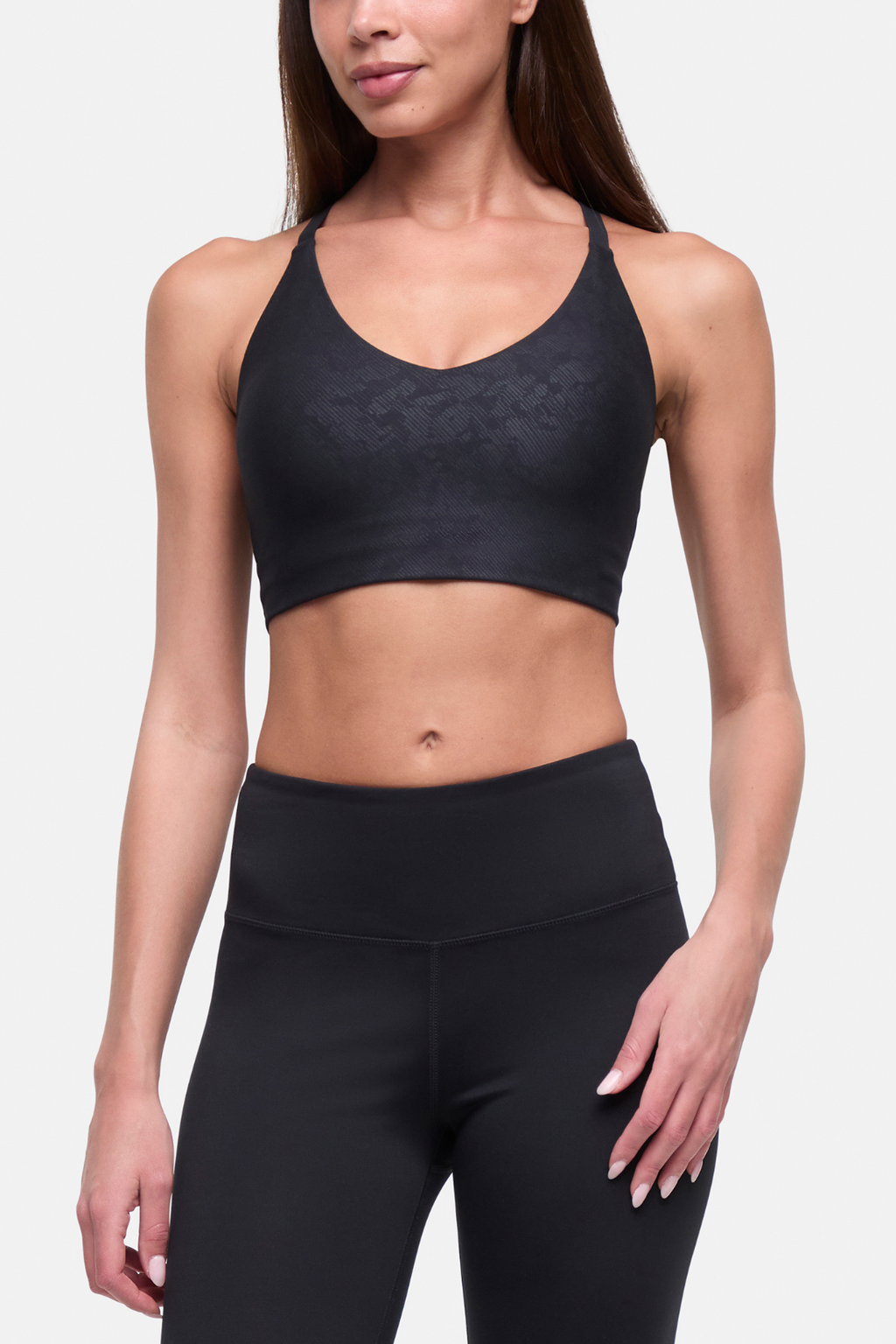 A woman modeling a black sports bra and matching high-waisted leggings against a light gray studio background. #color_black-linear-animal-camo