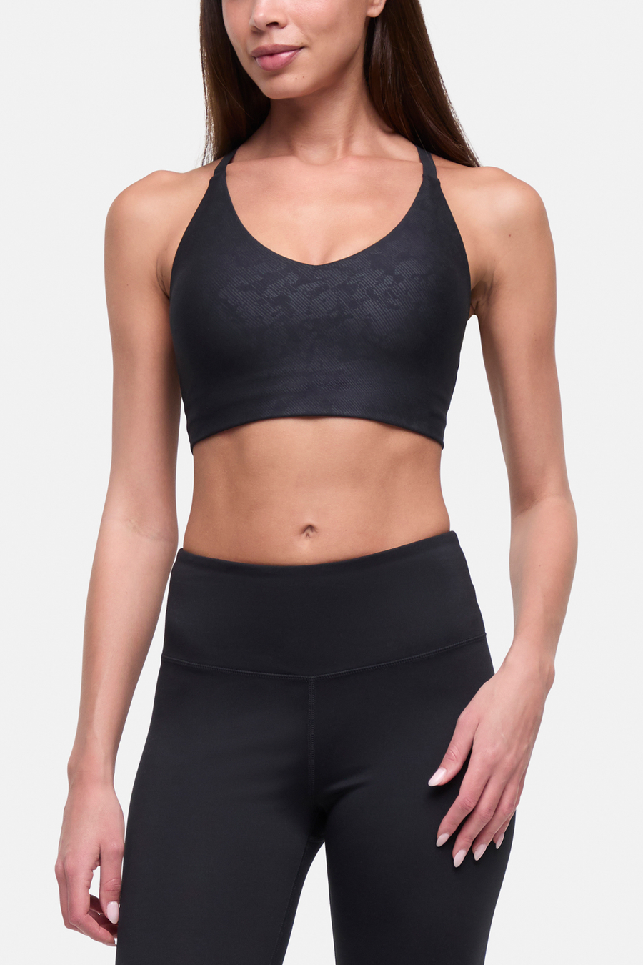 A woman modeling a black sports bra and matching high-waisted leggings against a light gray studio background. #color_black-linear-animal-camo