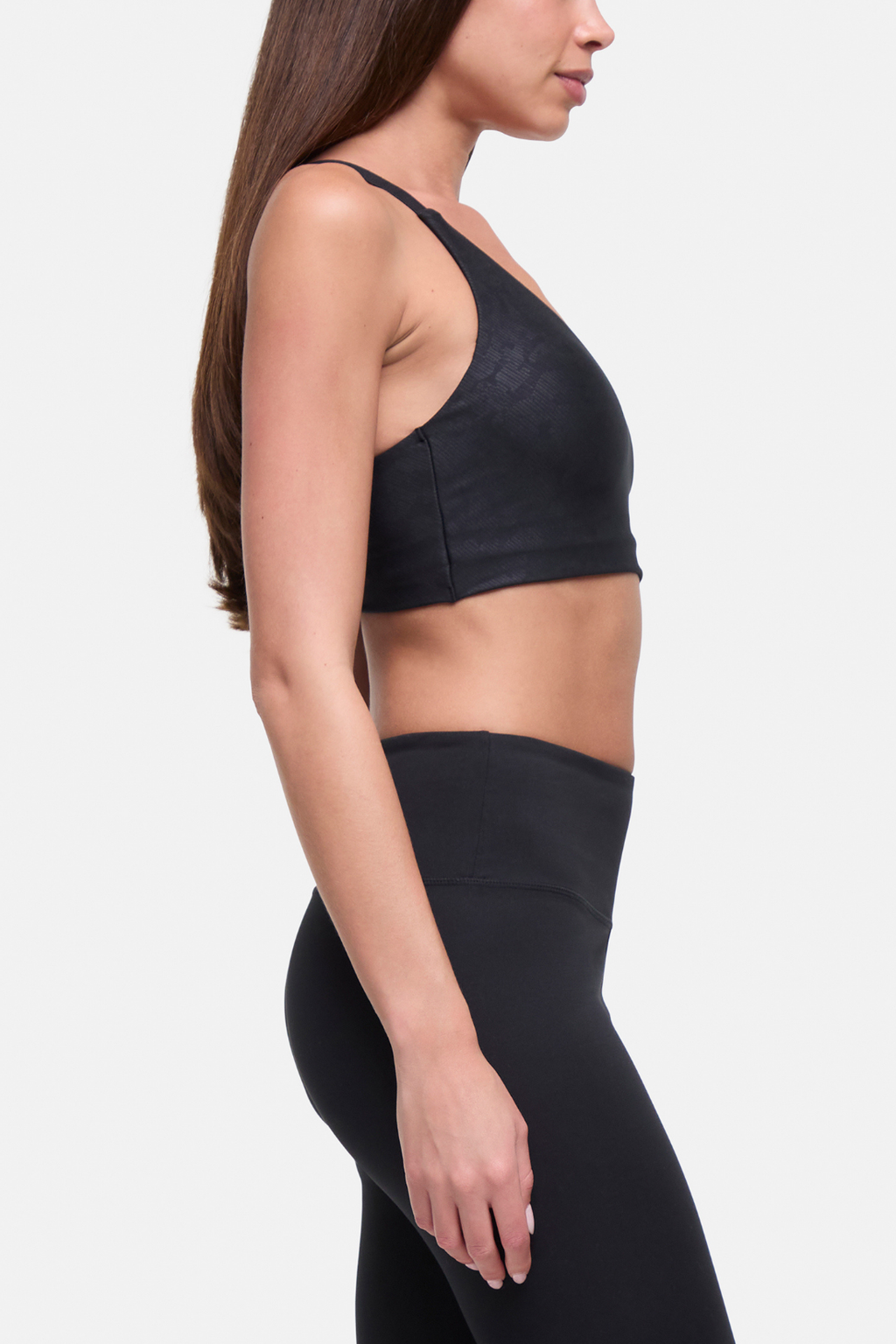 A woman shown in side profile wearing a black sports bra and matching black high-waisted leggings against a light gray studio background. #color_black-linear-animal-camo