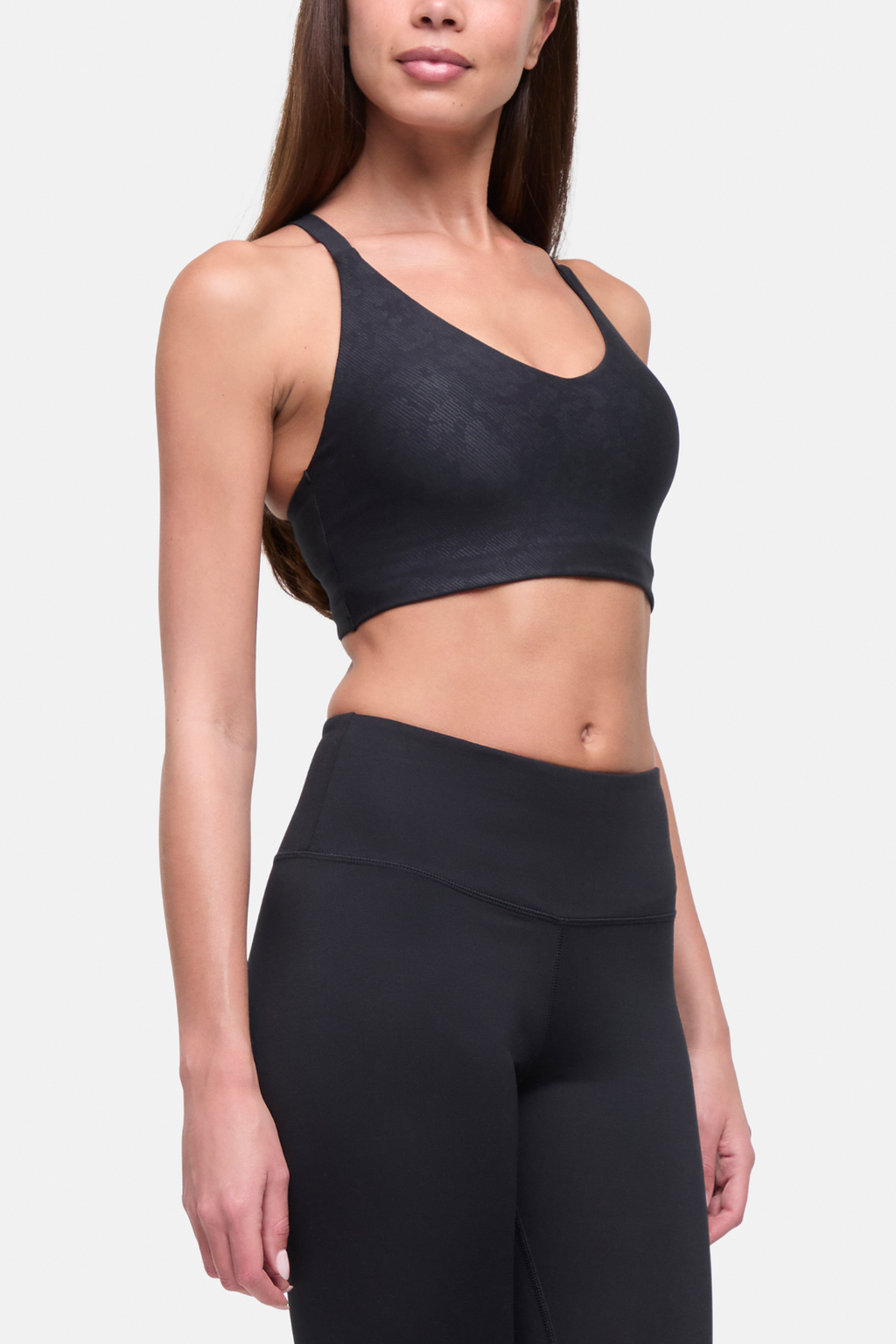 A woman modeling a black sports bra and matching high-waisted black leggings against a light gray studio background. #color_black-linear-animal-camo