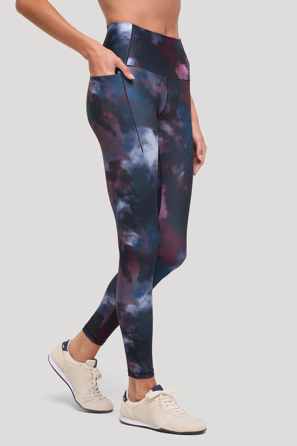 A model wearing high-waisted leggings with a dark blue, purple, and black galaxy cloud print, paired with beige sneakers, shown from the waist down against a solid light gray background. #color_winetasting-clouded-cause