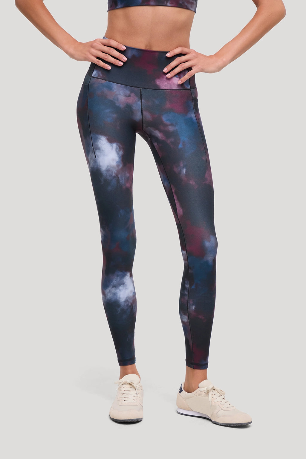 A model wearing high-waisted leggings with a dark navy, purple, and blue galaxy print, paired with a matching sports bra and beige sneakers, shown from the waist down on a light gray background. #color_winetasting-clouded-cause