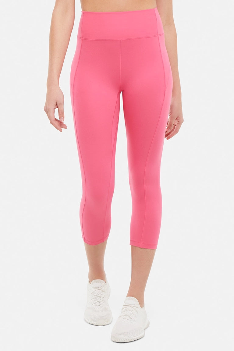 Front view of woman wearing pink capris and white sneakers on a light gray background. #color_pink-flambe