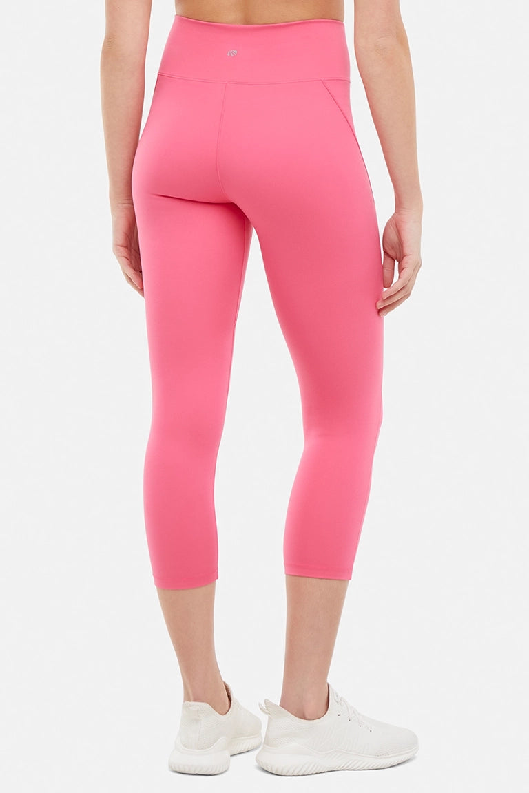 Back view of woman wearing pink capris and white sneakers on a light gray background. #color_pink-flambe