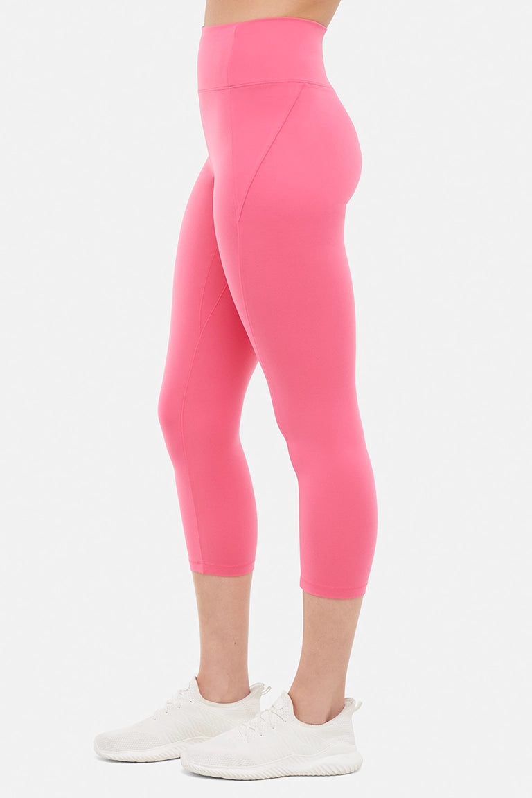 Side view of woman wearing pink capris and white sneakers on a light gray background. #color_pink-flambe