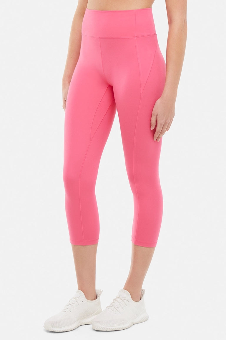 Front view of woman wearing pink capris and white sneakers on a light gray background. #color_pink-flambe