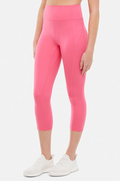 Front view of woman wearing pink capris and white sneakers on a light gray background. 