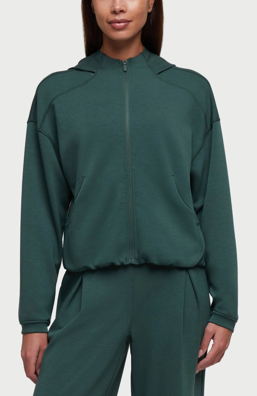 A woman wearing a dark green cropped zip-up hoodie with a high collar and matching sweatpants, shown against a plain white background. #color_garden-topiary