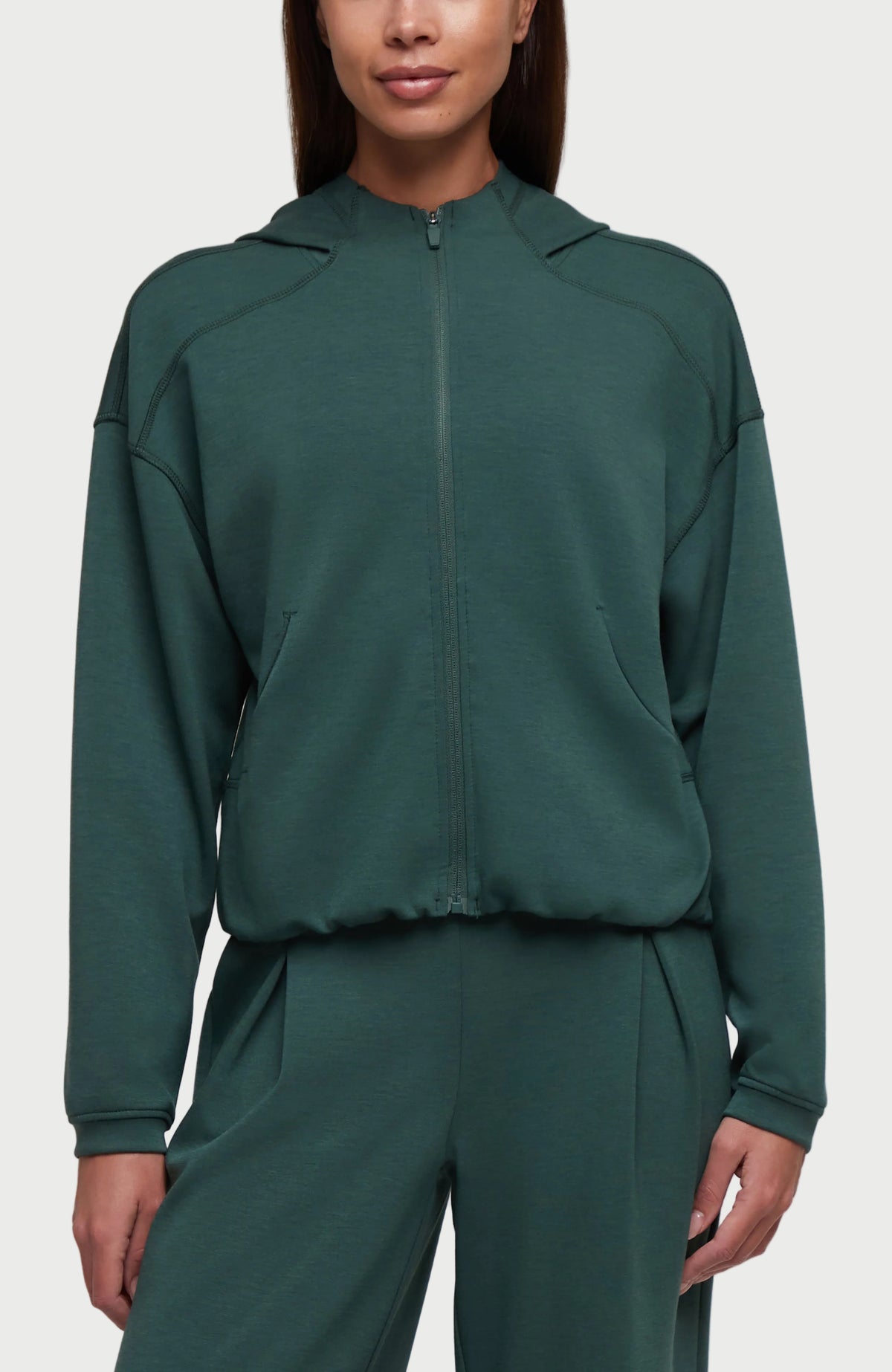 A woman wearing a dark green cropped zip-up hoodie with a high collar and matching sweatpants, shown against a plain white background. #color_garden-topiary