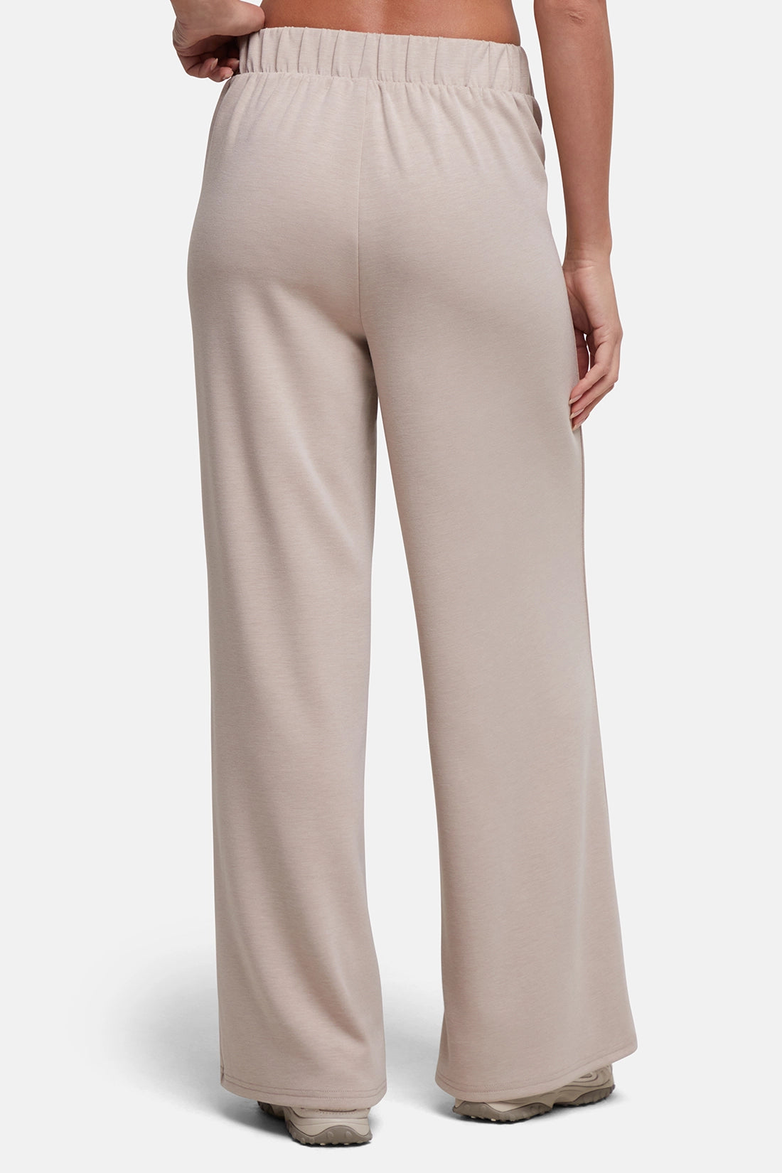 A person shown from the back wearing light beige wide-leg lounge pants with an elastic waistband, photographed against a clean light gray studio background. 