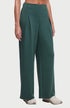 A model wearing a pair of wide-leg, high-waisted pants in a deep teal green color, paired with light gray sneakers, shown from the waist down on a grey studio background. 