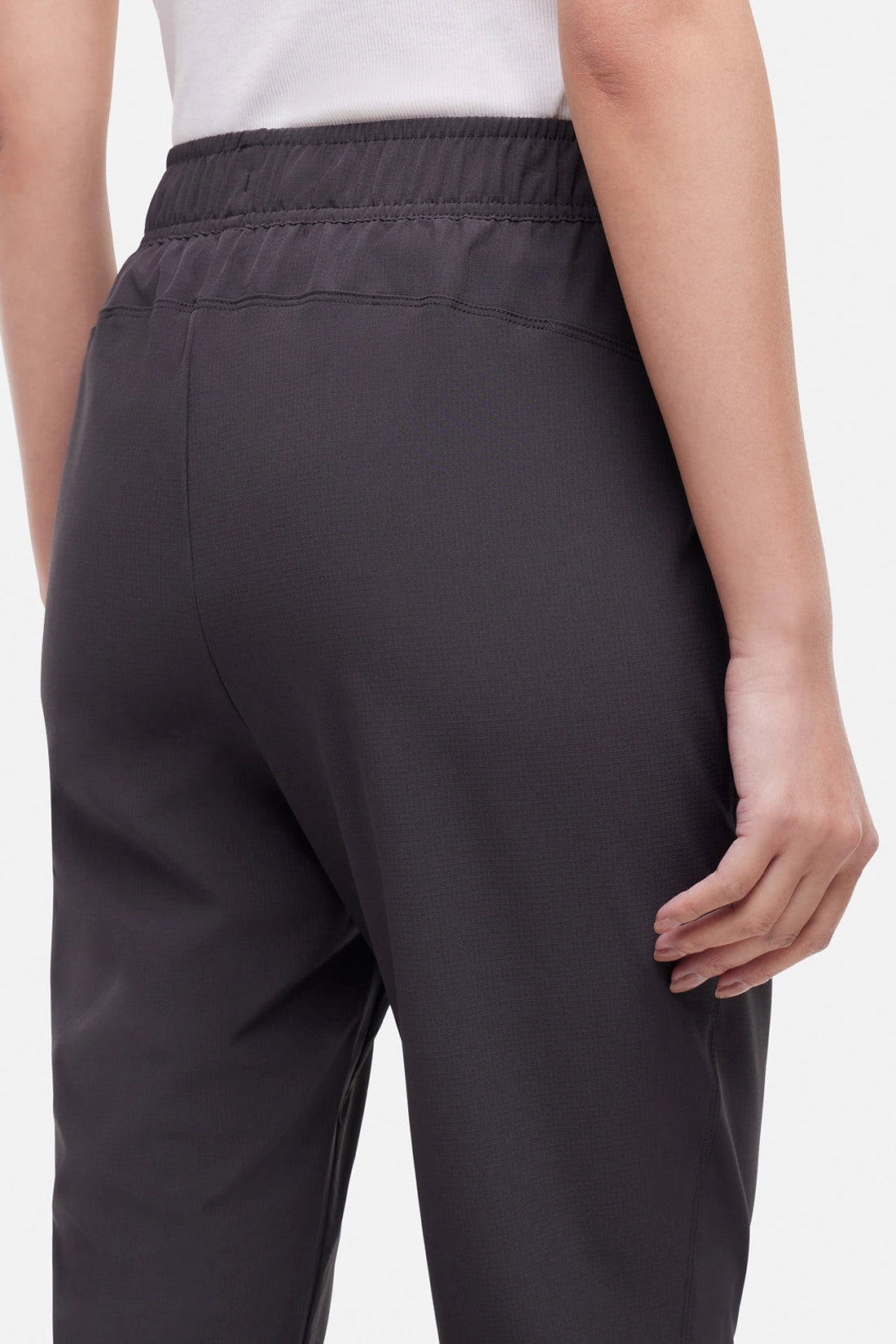 Close up back view of woman wearing black cropped pants with a white drawstring on a white background.