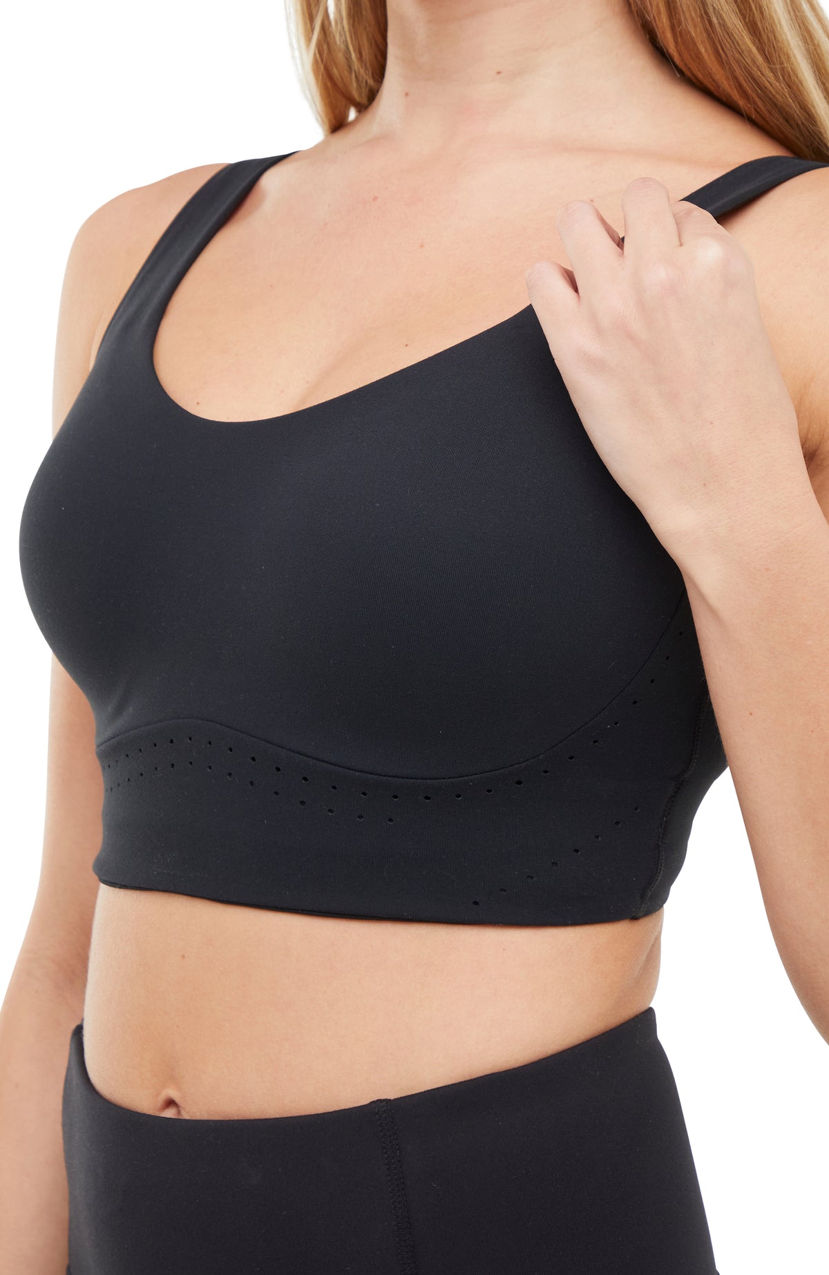 Close up front of woman wearing a black sports bra and matching black leggings on a white background.