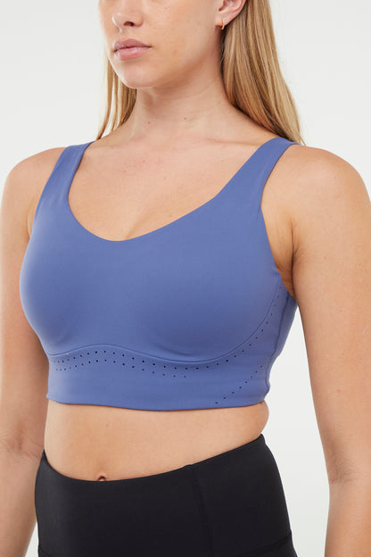 Close up of Woman wearing a blue sports bra and black leggings on a white background. 