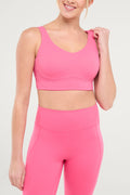 Front view of woman wearing a pink sports bra and matching pink leggings on a white background. #color_pink-flambe